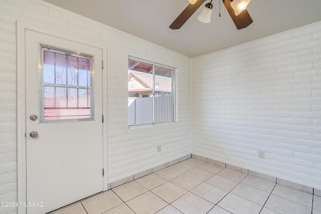 empty room featuring a ceiling fan, light tile patterned flooring, and brick wall