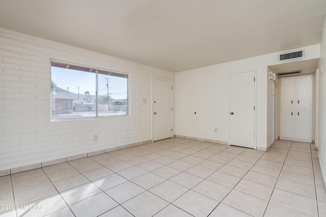 spare room with visible vents, brick wall, and light tile patterned flooring