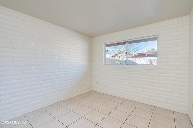 empty room featuring brick wall and light tile patterned flooring