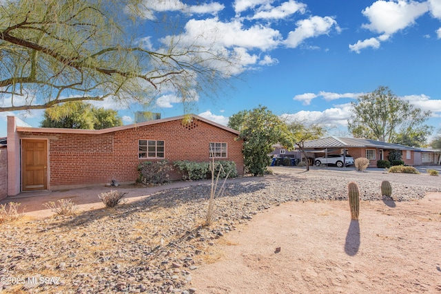 view of side of home featuring driveway, a carport, and brick siding