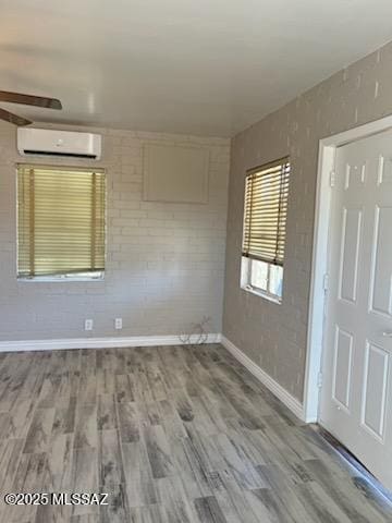 unfurnished room featuring a wall mounted air conditioner, baseboards, and wood finished floors