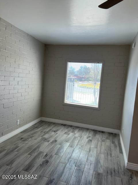 spare room with ceiling fan, brick wall, baseboards, and wood finished floors