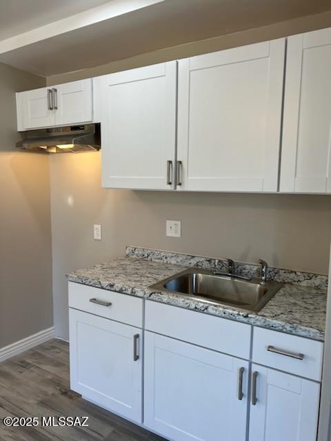 kitchen with under cabinet range hood, white cabinetry, light stone counters, and a sink