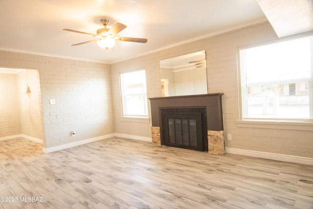 unfurnished living room featuring a glass covered fireplace, crown molding, a ceiling fan, and wood finished floors
