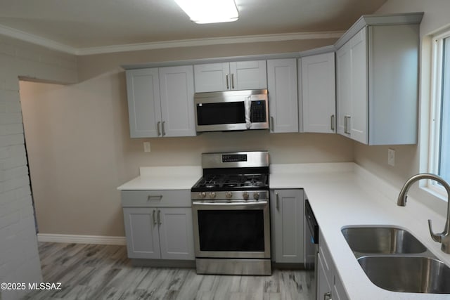 kitchen featuring light wood-type flooring, a sink, appliances with stainless steel finishes, crown molding, and light countertops