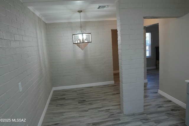 unfurnished dining area with wood finished floors, visible vents, brick wall, baseboards, and crown molding