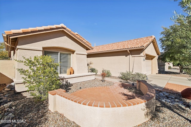 rear view of house featuring an attached garage, a tile roof, and stucco siding