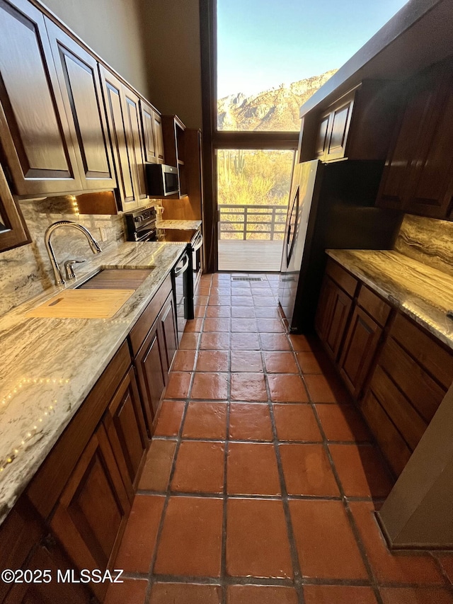 kitchen with light stone countertops, dark tile patterned flooring, a sink, decorative backsplash, and appliances with stainless steel finishes