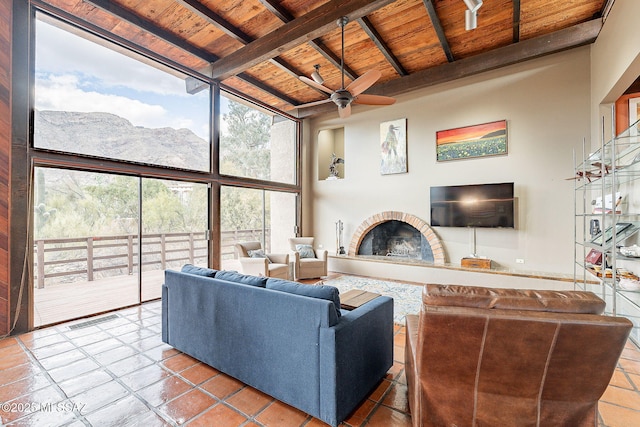 living area featuring beam ceiling, a high ceiling, floor to ceiling windows, a glass covered fireplace, and wooden ceiling