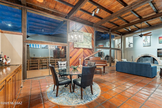 tiled dining space featuring ceiling fan with notable chandelier, wooden ceiling, a fireplace, and beam ceiling