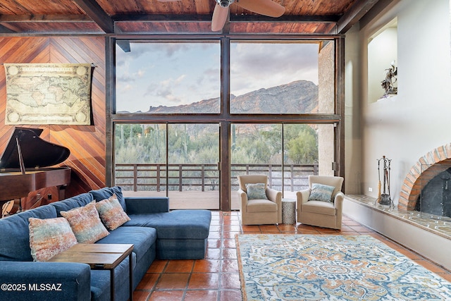 tiled living area featuring wooden walls, a fireplace with raised hearth, expansive windows, wooden ceiling, and beamed ceiling