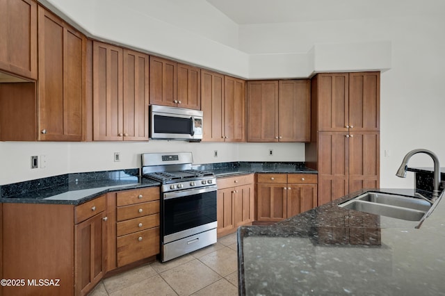 kitchen featuring dark stone counters, stainless steel appliances, brown cabinetry, and a sink