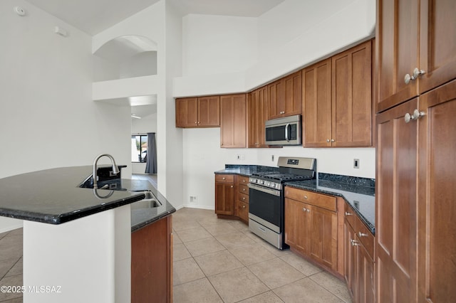 kitchen with stainless steel appliances, brown cabinets, a sink, and dark stone countertops