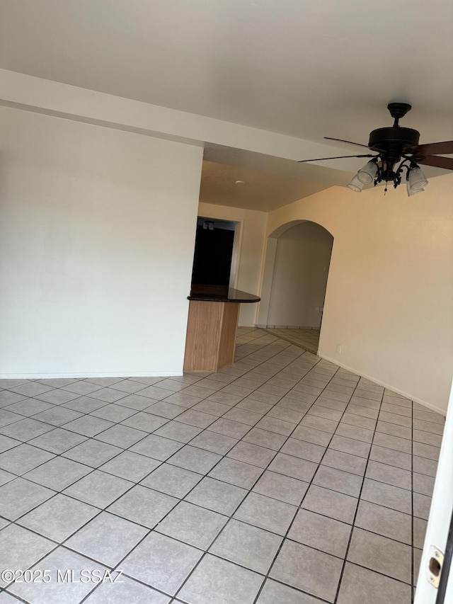 empty room featuring light tile patterned floors, ceiling fan, and arched walkways