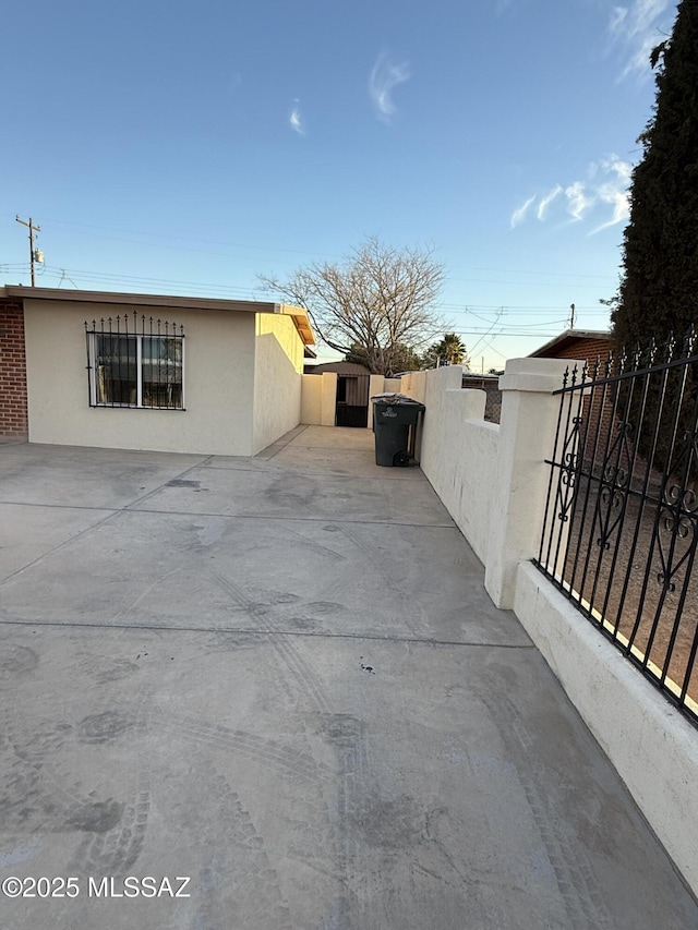 view of property exterior featuring a gate, a patio area, fence, and stucco siding