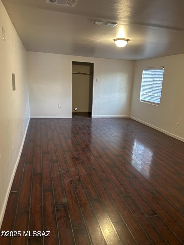 empty room with dark wood-style flooring, visible vents, and baseboards