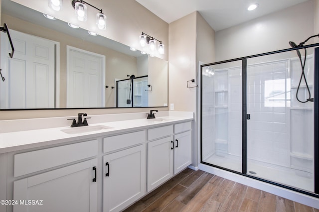 full bathroom with a stall shower, double vanity, a sink, and wood finished floors