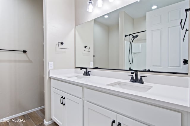 full bathroom with double vanity, walk in shower, a sink, and wood finished floors