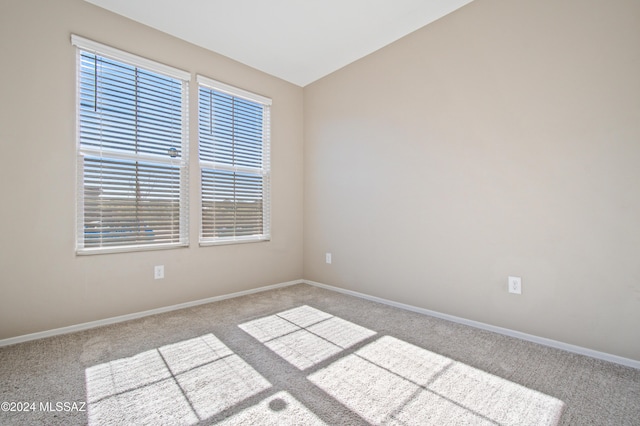 spare room featuring light carpet, vaulted ceiling, and baseboards