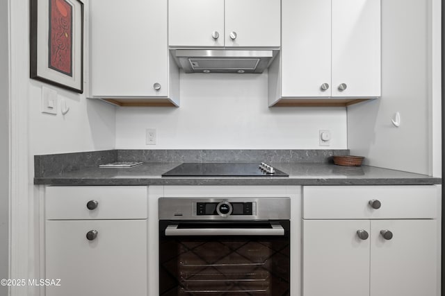 kitchen featuring range hood, black electric stovetop, dark countertops, white cabinetry, and oven