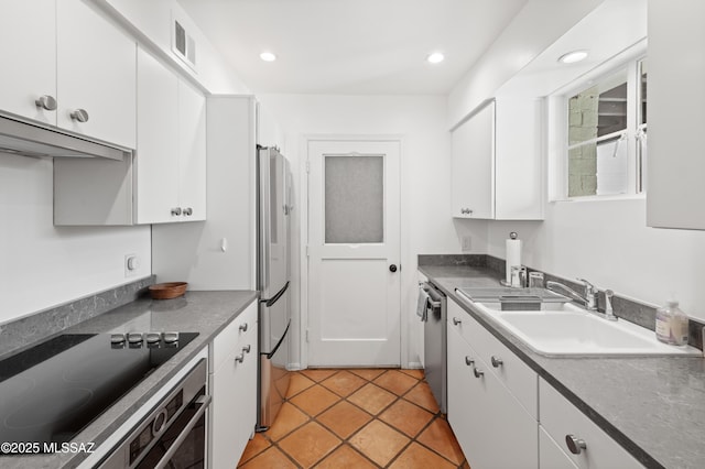 kitchen featuring stainless steel appliances, dark countertops, white cabinetry, and a sink