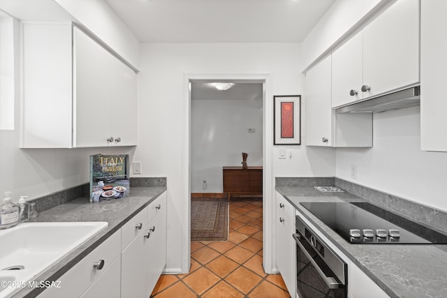 kitchen featuring black electric stovetop, white cabinets, a sink, and oven