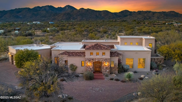 back of house featuring stone siding, decorative driveway, a mountain view, and stucco siding