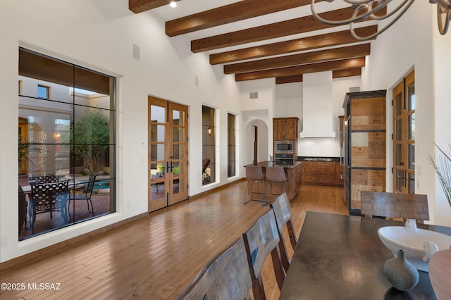 dining room with arched walkways, french doors, a high ceiling, dark wood-type flooring, and beamed ceiling