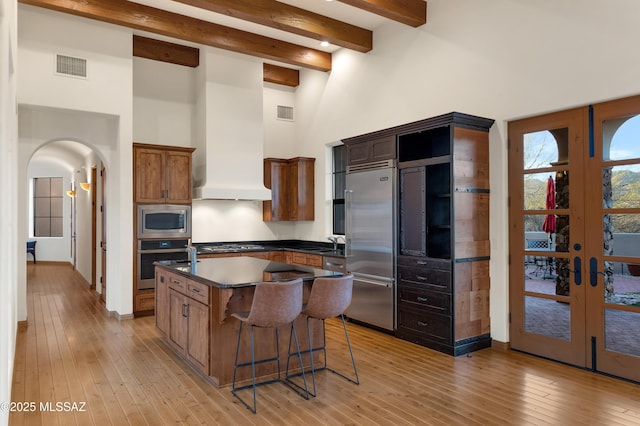 kitchen with a center island, arched walkways, dark countertops, visible vents, and built in appliances