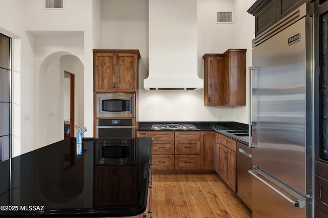 kitchen featuring visible vents, custom range hood, light wood-style flooring, and built in appliances