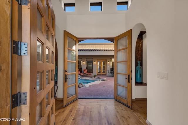 doorway to outside with french doors, light wood-type flooring, and a high ceiling