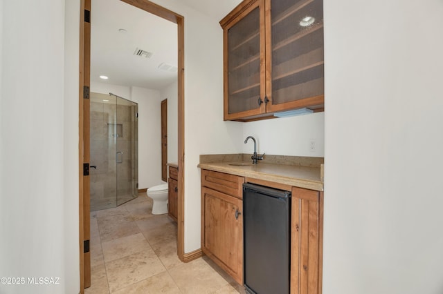 kitchen with brown cabinets, light countertops, visible vents, glass insert cabinets, and a sink