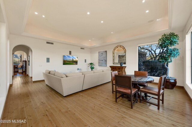 living room with arched walkways, a tray ceiling, visible vents, and light wood-style flooring