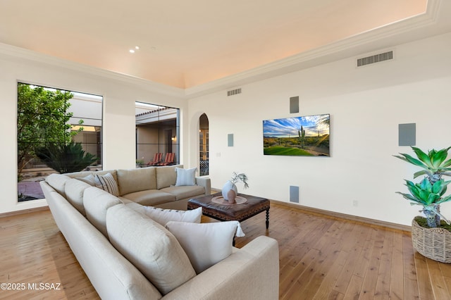 living area featuring arched walkways, light wood-style flooring, ornamental molding, and visible vents