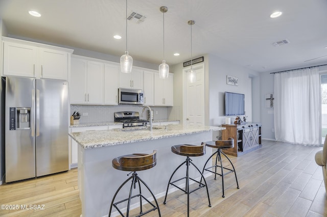 kitchen with stainless steel appliances, a sink, visible vents, white cabinets, and an island with sink