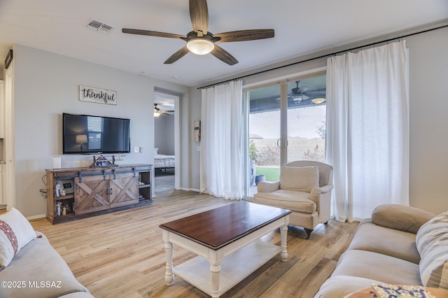 living room featuring baseboards, a ceiling fan, visible vents, and light wood-style floors