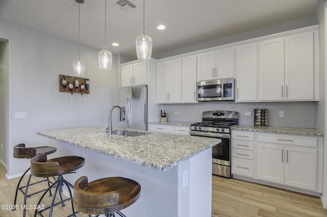 kitchen with visible vents, hanging light fixtures, appliances with stainless steel finishes, a kitchen island with sink, and white cabinets