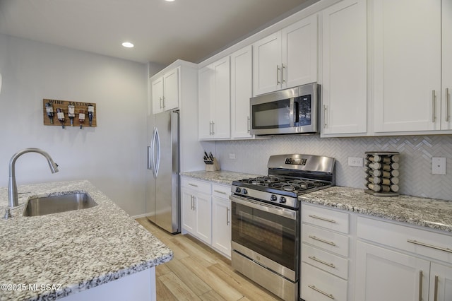 kitchen with light stone counters, a sink, stainless steel appliances, white cabinetry, and backsplash