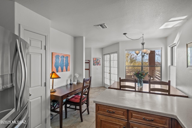 kitchen featuring light countertops, visible vents, stainless steel fridge, and decorative light fixtures