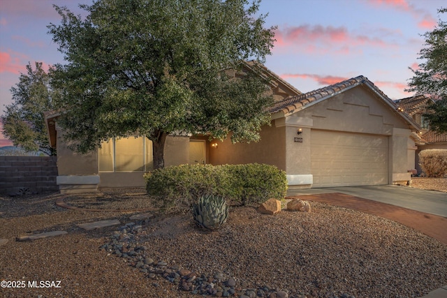 view of property hidden behind natural elements featuring a garage, a tiled roof, concrete driveway, and stucco siding