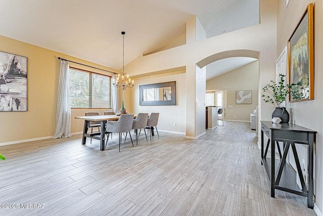 dining room featuring arched walkways, light wood finished floors, an inviting chandelier, high vaulted ceiling, and baseboards