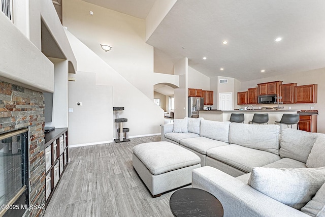 living room with arched walkways, visible vents, a glass covered fireplace, high vaulted ceiling, and baseboards