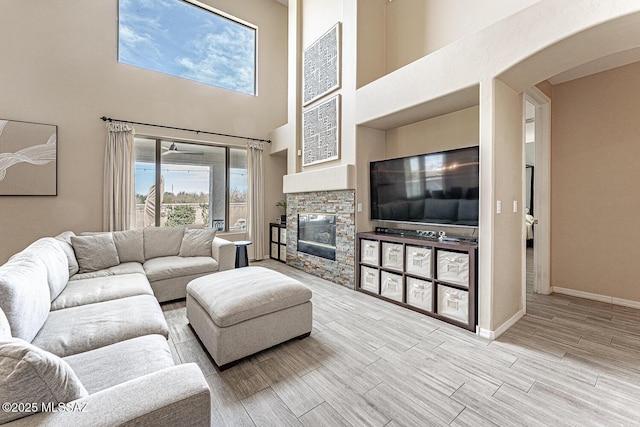 living area featuring arched walkways, a stone fireplace, baseboards, and wood tiled floor