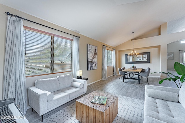 living area with lofted ceiling, light wood finished floors, baseboards, and a notable chandelier