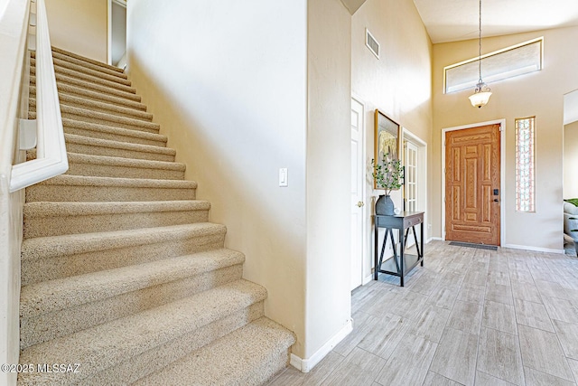 foyer entrance with baseboards, visible vents, stairway, wood finished floors, and a high ceiling