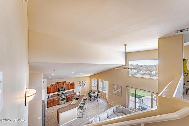 living room featuring high vaulted ceiling, light wood-style floors, visible vents, and a ceiling fan