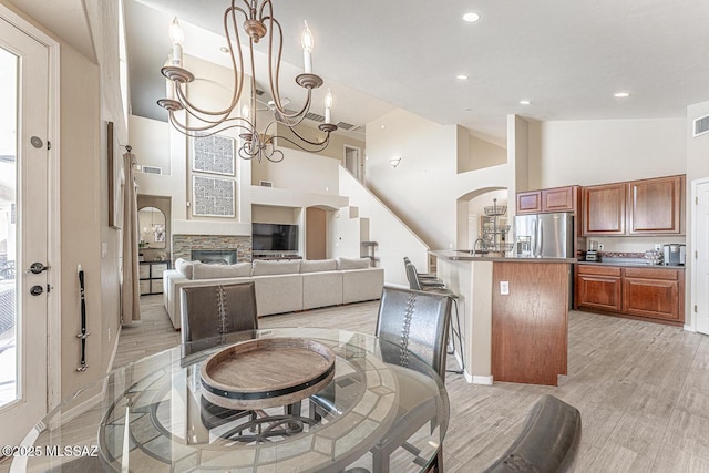 dining space featuring visible vents, light wood-style flooring, a stone fireplace, high vaulted ceiling, and a notable chandelier