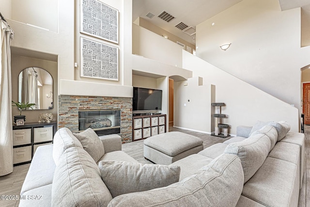 living room featuring visible vents, a towering ceiling, a stone fireplace, wood finished floors, and baseboards