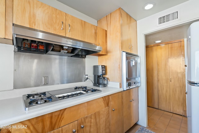 kitchen with gas stovetop, light countertops, visible vents, freestanding refrigerator, and ventilation hood