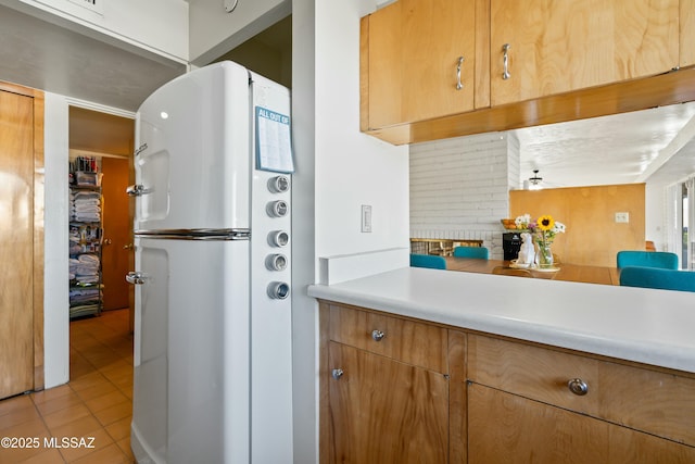 kitchen with light tile patterned floors, light countertops, freestanding refrigerator, decorative backsplash, and brown cabinetry